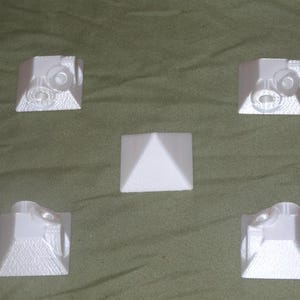 May include: Five white 3D printed pyramid-shaped objects. Four of the pyramids have a design on each side. One pyramid is plain.