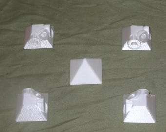 Puede incluir: Cinco objetos de forma piramidal impresos en 3D de color blanco. Cuatro de las pirámides tienen un diseño en cada lado. Una pirámide es lisa.