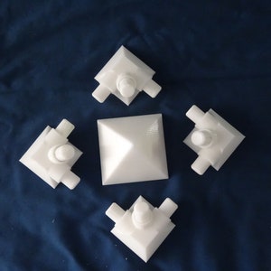 May include: Four white plastic corner pieces with a white pyramid in the centre. The corner pieces have a small round knob on top.