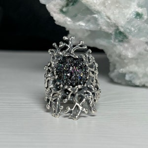 May include: A silver ring with a black gemstone surrounded by a delicate, intricate design resembling branches or coral.