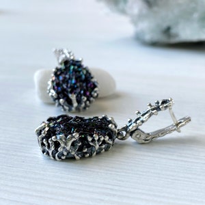 May include: A pair of silver earrings with iridescent black gemstone drops. The earrings have a delicate, intricate design and are perfect for adding a touch of sparkle to any outfit.