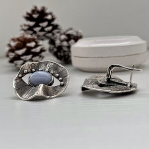 Puede incluir: Un par de pendientes de plata con una piedra de &aacute;gata azul engastada en un dise&ntilde;o texturizado en forma de ojo. Los pendientes tienen un cierre de gancho.