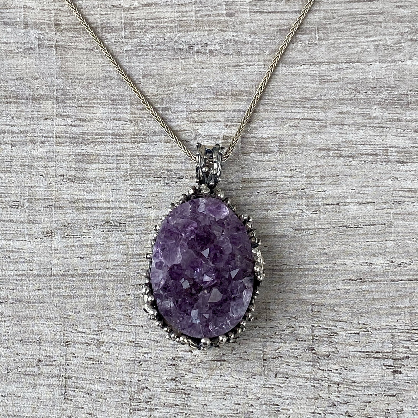 Large raw amethyst druzy pendant necklace set in sterling silver on textured wooden background.