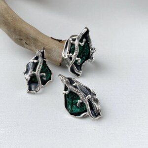 May include: A set of silver earrings and a ring featuring a green malachite stone with a silver lizard design.