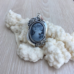 May include: A silver cameo pendant with a black and white cameo of a woman's profile. The pendant is decorated with small silver beads and has a detailed design.