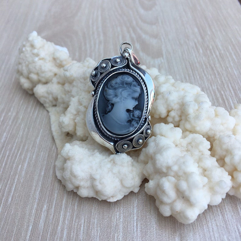 May include: A silver cameo pendant with a black and white cameo of a woman's profile. The pendant is decorated with small silver beads and has a detailed design.