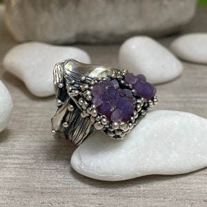 May include: A silver ring with a textured design and a cluster of purple amethyst stones.