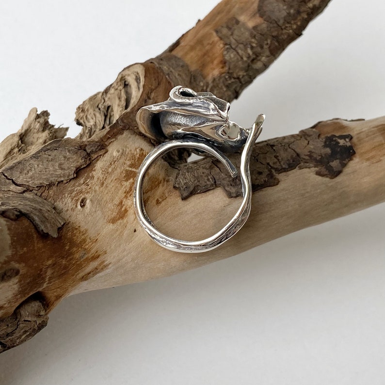 May include: A silver ring with a textured, organic design. The ring is open and has a wide band.
