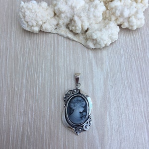 May include: A silver cameo pendant with a black and white portrait of a woman. The pendant has a detailed design with floral accents.