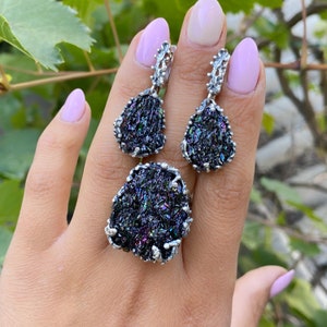 May include: A set of silver earrings and a ring featuring iridescent black gemstone accents. The earrings are teardrop shaped and the ring is a statement piece.