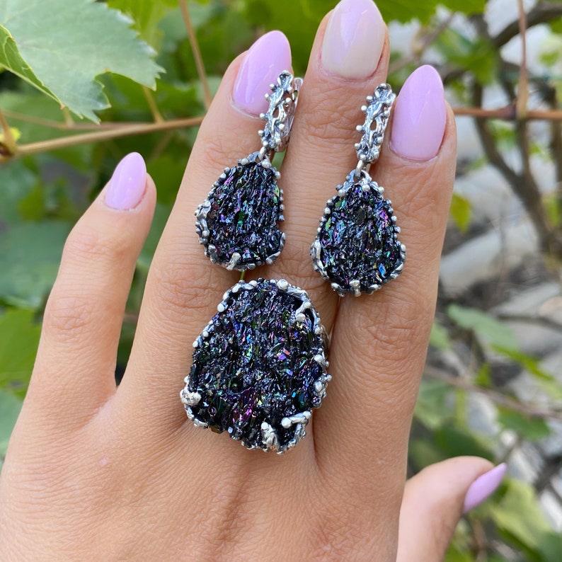 May include: A set of silver earrings and a ring featuring iridescent black gemstone accents. The earrings are teardrop shaped and the ring is a statement piece.