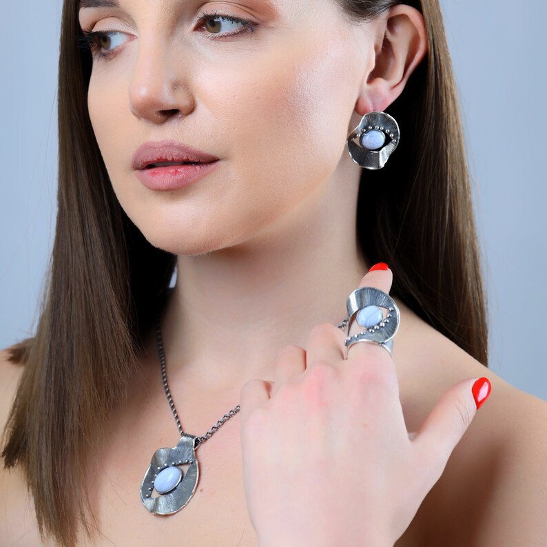 Puede incluir: Un conjunto de collar, anillo y pendientes de plata con una piedra de &aacute;gata azul. Las joyas presentan un dise&ntilde;o &uacute;nico y org&aacute;nico con un acabado texturizado.