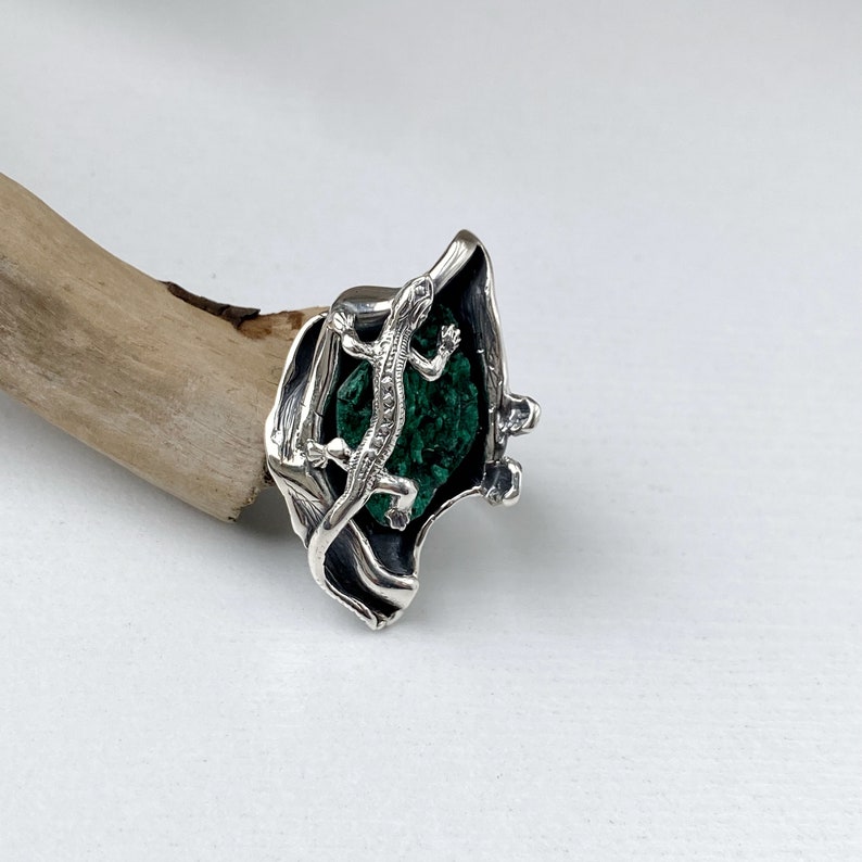 May include: A silver ring with a green malachite stone and a detailed lizard design.