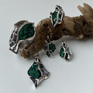 May include: A silver jewelry set featuring a bracelet, necklace, and earrings. Each piece has a green malachite stone set in a silver lizard design.