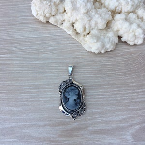 May include: A silver pendant with a black cameo featuring a woman's profile. The pendant has a detailed design with small silver beads and swirls.