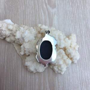 May include: Silver pendant with a black oval stone. The pendant has a detailed design around the stone.