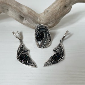 May include: A set of silver earrings and a ring with a black iridescent stone. The jewelry has a unique, organic design with intricate details.
