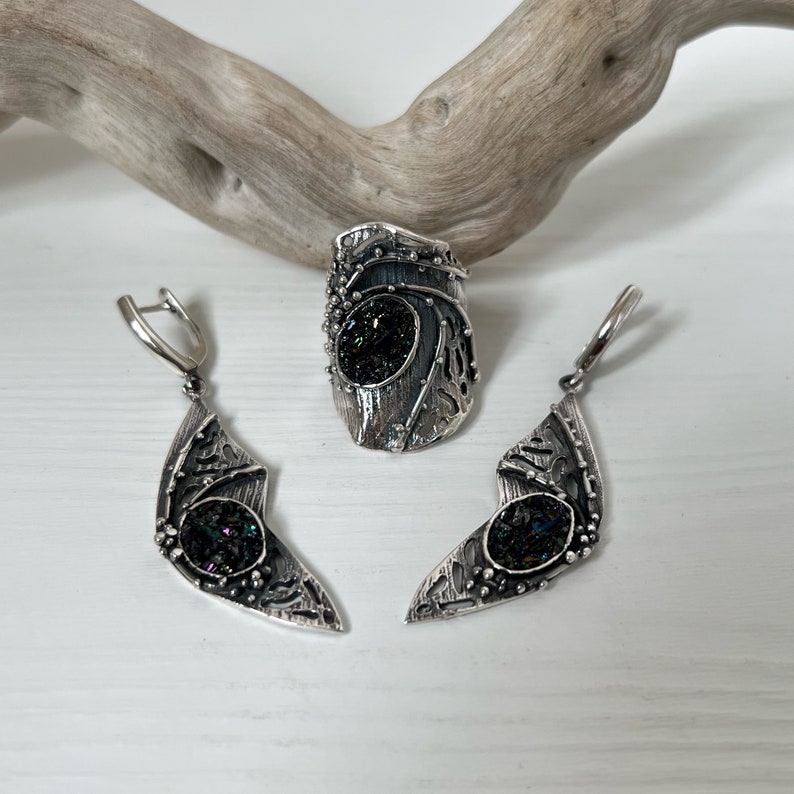May include: A set of silver earrings and a ring with a black iridescent stone. The jewelry has a unique, organic design with intricate details.