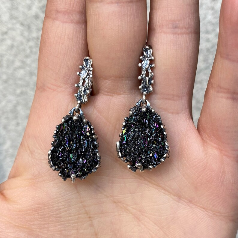 May include: A pair of silver earrings with black iridescent gemstone drops. The earrings have a delicate, intricate design.