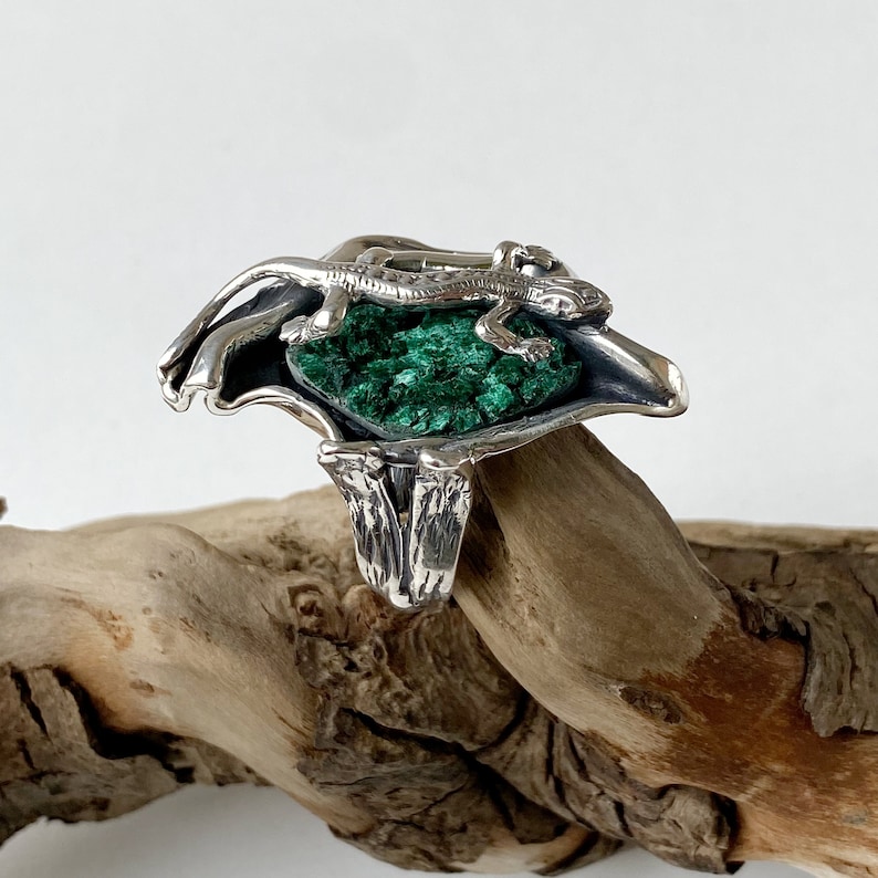 May include: A silver ring with a green malachite stone and a lizard design.