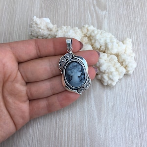 May include: A silver cameo pendant with a black and white portrait of a woman. The pendant has a detailed design with a rope border and small decorative circles.