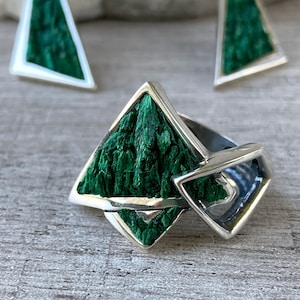 May include: A silver ring featuring a green malachite stone set in a geometric design. The ring is crafted from two intersecting triangular shapes.