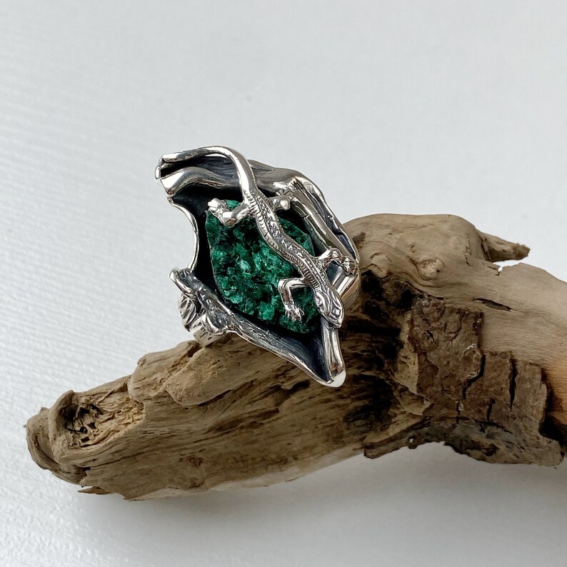 May include: A silver ring with a green malachite stone and a detailed lizard design.