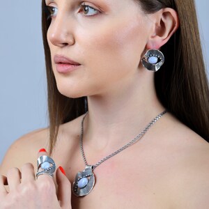 Puede incluir: Un conjunto de collar, anillo y pendientes de plata con un colgante de piedra azul. Las joyas presentan un dise&ntilde;o &uacute;nico y org&aacute;nico con un acabado texturizado.