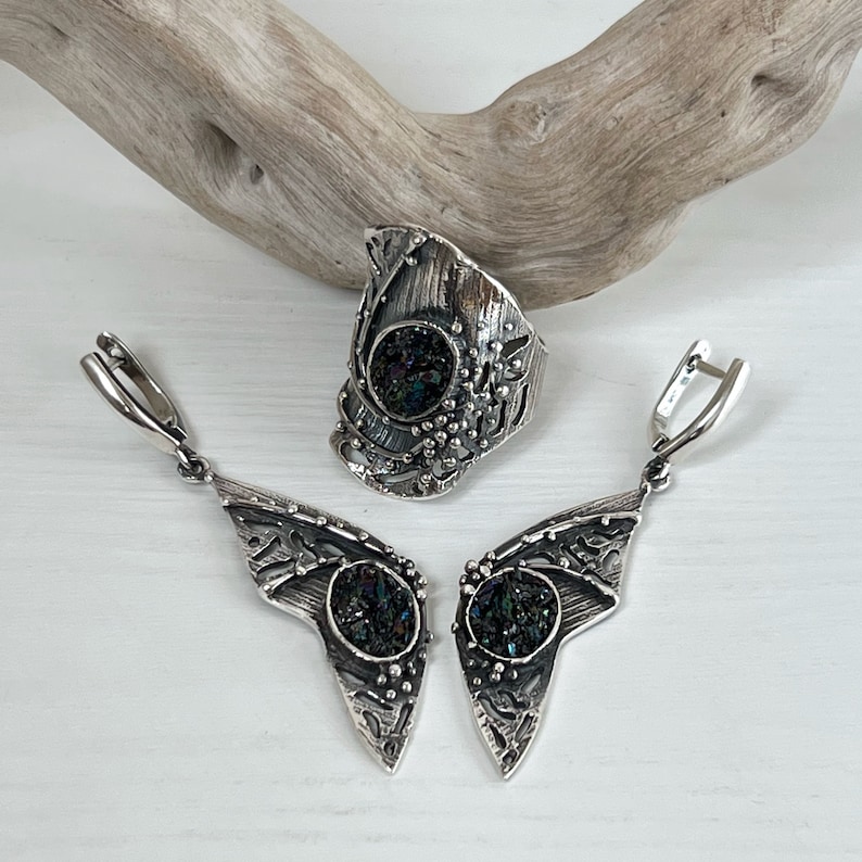 May include: A silver ring and earrings set with a black iridescent stone. The ring is a wide band with a textured design and the earrings are long and dangle.