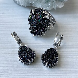 May include: A silver ring and earrings set featuring iridescent black gemstone accents. The ring and earrings have a unique, organic design with a branch-like pattern.