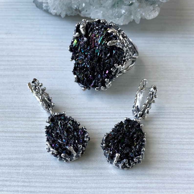 May include: A silver ring and earrings set featuring iridescent black gemstone accents. The ring and earrings have a unique, organic design with a branch-like pattern.