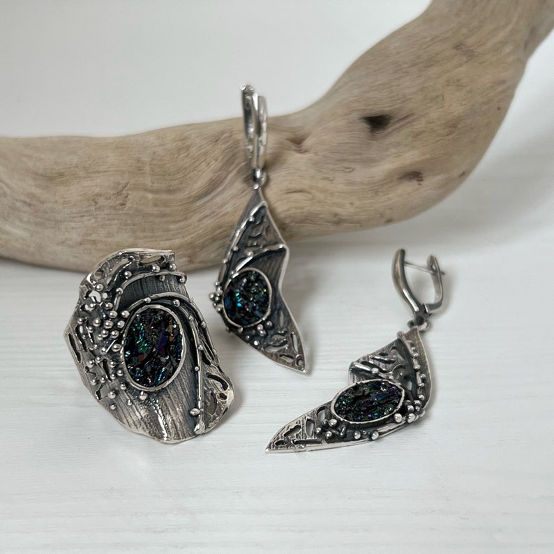 May include: A silver ring and earrings set with a dark green iridescent stone. The jewelry features intricate designs and a textured finish.