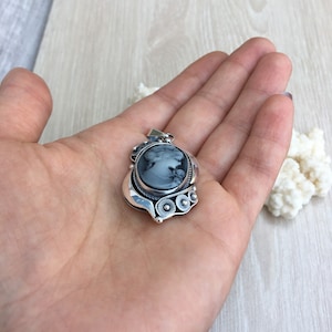 May include: A silver pendant with a black cameo featuring a woman's profile. The pendant has a detailed design with a swirl pattern and three round accents.