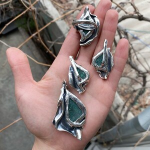 May include: Three silver pendant necklaces with green stone accents. The pendants are shaped like leaves with intricate details.