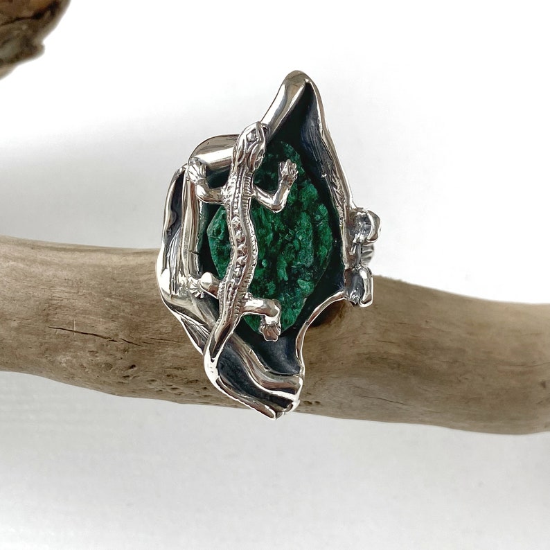 May include: A silver ring with a green malachite stone and a detailed lizard design.