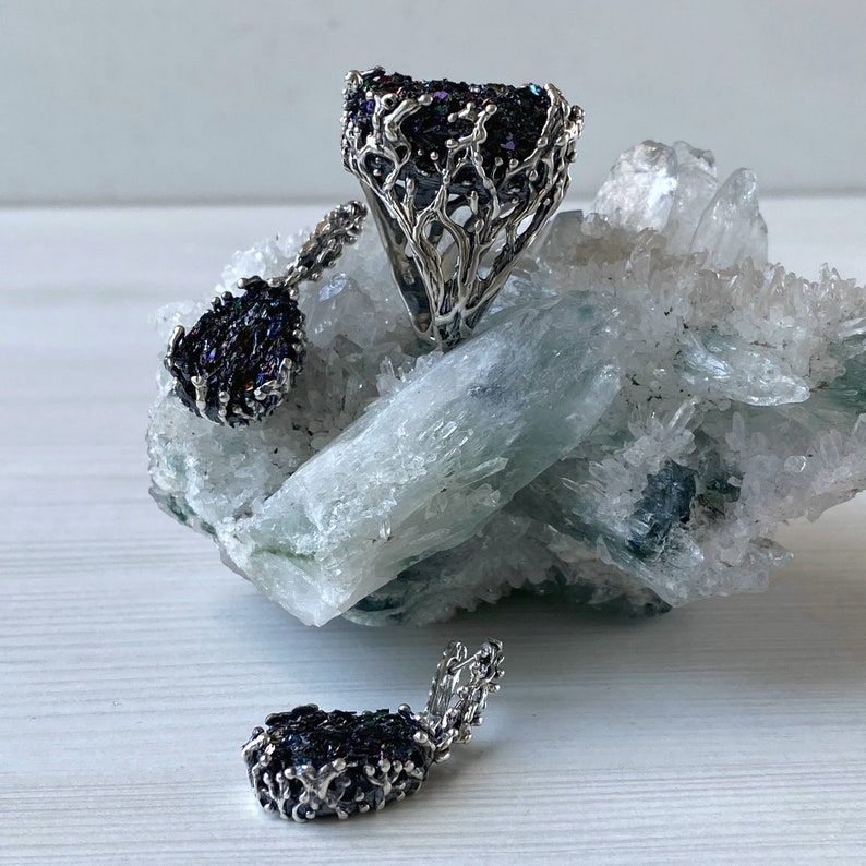 May include: A set of three silver rings with black gemstone accents. The rings are displayed on a bed of white crystals.