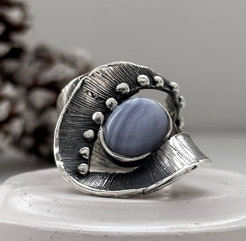 Puede incluir: Un anillo de plata con una banda texturizada y una piedra de &aacute;gata azul engastada en el centro.