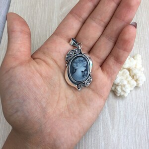 May include: A silver pendant featuring a cameo of a woman's profile in black and white. The cameo is surrounded by a silver filigree design.
