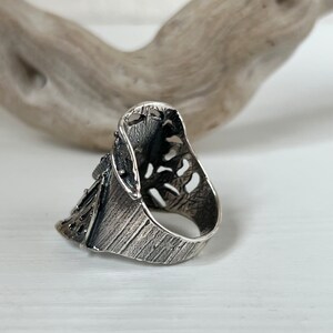 May include: A silver ring with an intricate, openwork design. The ring is made of a textured metal and has a unique, asymmetrical shape.