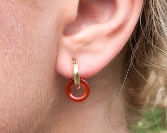 May include: Gold hoop earrings with a red carnelian stone accent. The earrings are a simple and elegant design.