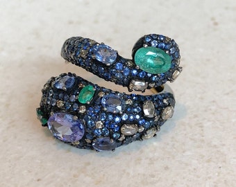 May include: A silver ring with a swirling design set with blue sapphires, green emeralds, and white diamonds.