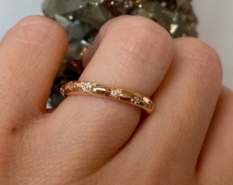 May include: A gold band ring with small diamonds set in a row around the band.