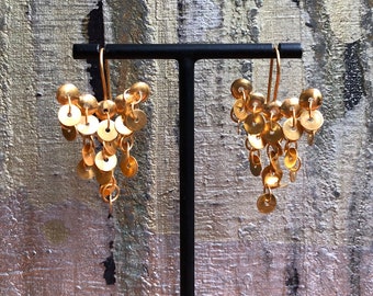 May include: A pair of gold dangle earrings with multiple round discs hanging from the bottom. The earrings are displayed on a black stand.