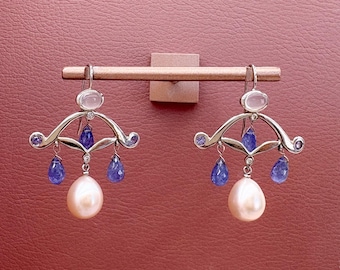 May include: A pair of silver dangle earrings with a teardrop-shaped pearl, blue gemstones, and a pink stone at the top.