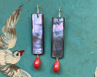 May include: A pair of long, rectangular earrings with a dark iridescent finish and a dangling red teardrop-shaped stone.