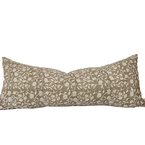 May include: A long, rectangular pillow with a floral pattern. The pillow has a muted green background with a cream-colored floral design. The pillow is a decorative item for a bed or sofa.
