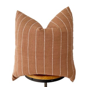 May include: A brown throw pillow with white vertical stripes. The pillow is made of a soft, textured fabric and has a subtle sheen.