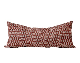 May include: A long, rectangular cushion with a rust-coloured fabric featuring a white floral pattern.