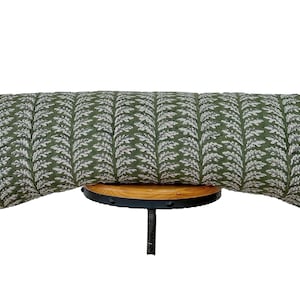 May include: A long, rectangular decorative pillow with a green and white leaf pattern. The pillow is approximately 30 inches long and rests on a small, round wooden surface with a black metal base. The pillow's fabric has a textured appearance.