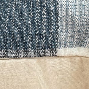 May include: Close-up of a blue and white patterned fabric with a white canvas backing. The fabric has a woven texture and a geometric design.